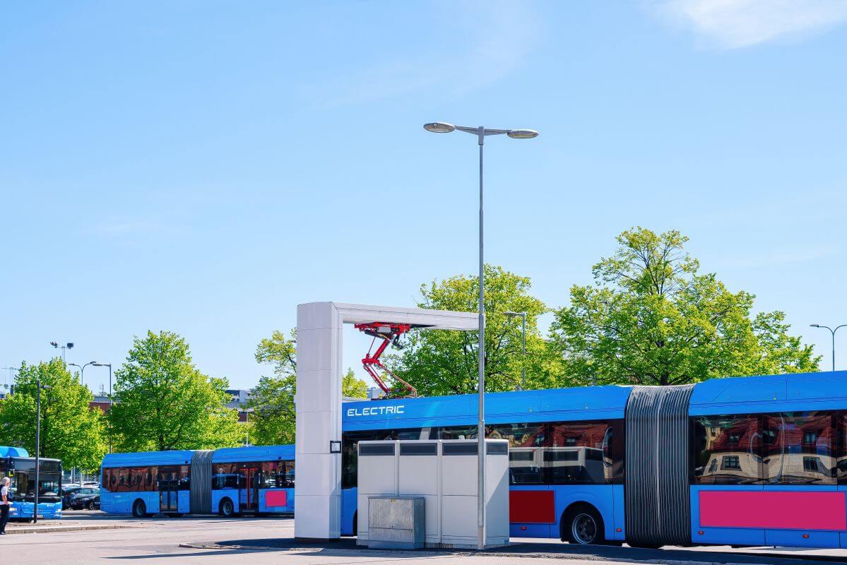 Autobusy elektryczne korzystające ze stacji ładowania autobusów elektrycznych na tle zielonych drzew.