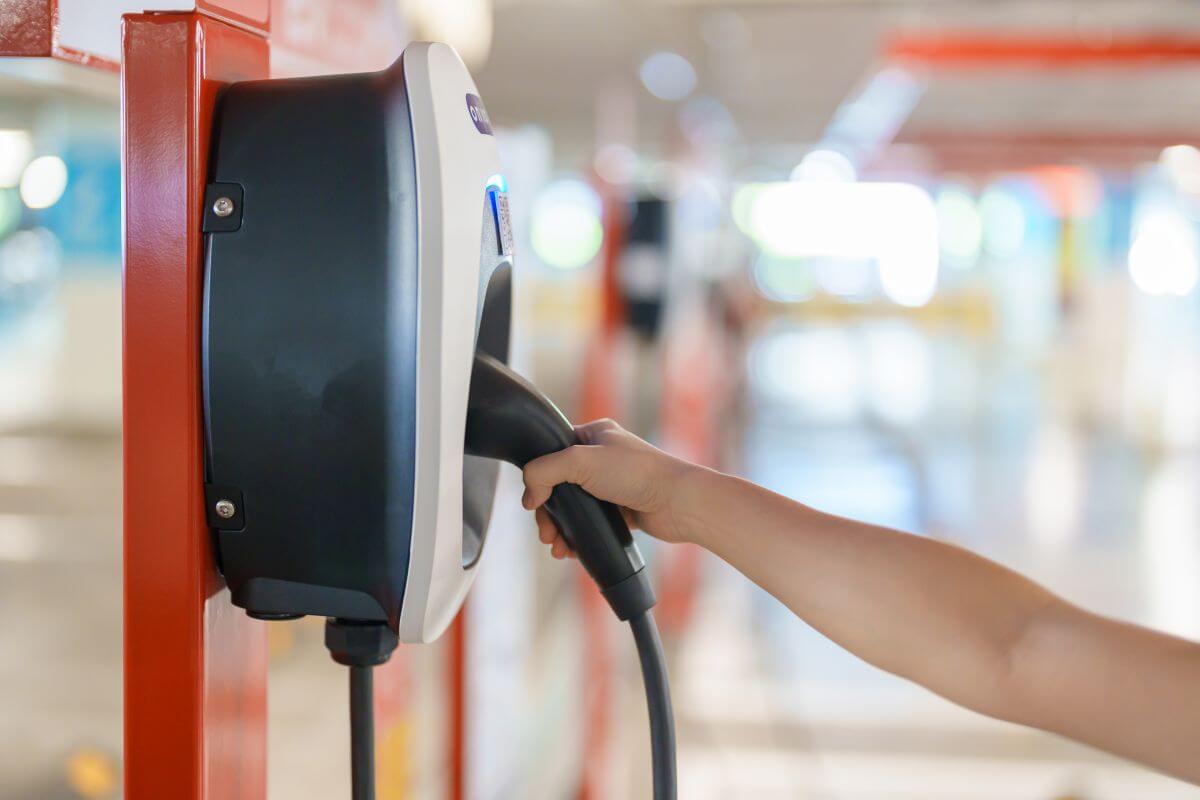 Ręka trzyma wtyczkę przy stacje ładowania samochodów elektrycznych.