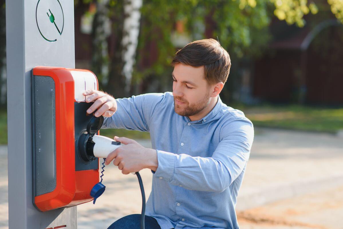 Mężczyzna korzysta z serwisu stacji ładowania samochodów elektrycznych, podłączając pojazd do ładowarki.