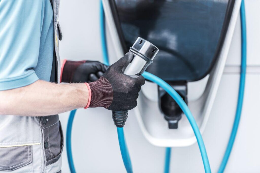 Mężczyzna w rękawicach trzyma kabel podczas instalacji stacji ładowania samochodów elektrycznych.