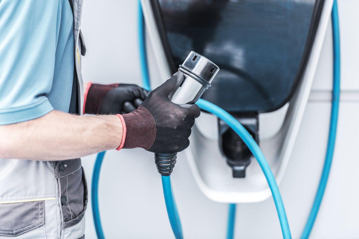 Mężczyzna w rękawicach trzyma kabel podczas instalacji stacji ładowania samochodów elektrycznych.