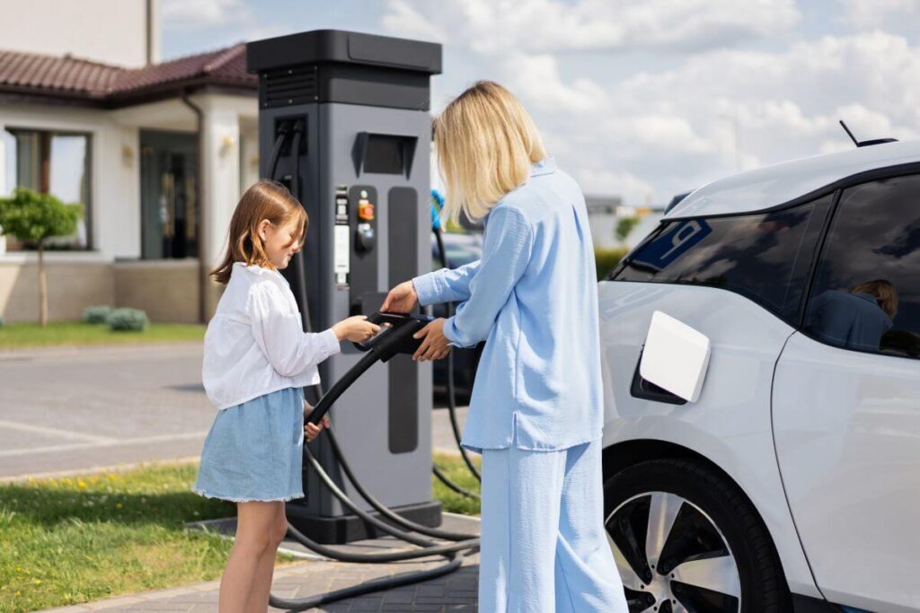 Matka z córką podłączają samochód elektryczny do ładowarki podczas instalacji stacji ładowania samochodów elektrycznych.